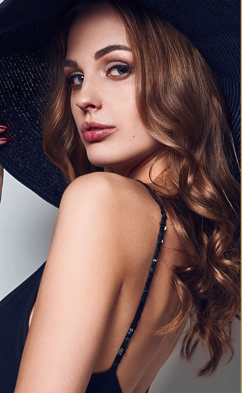 Woman in hat with curled hair and makeup.