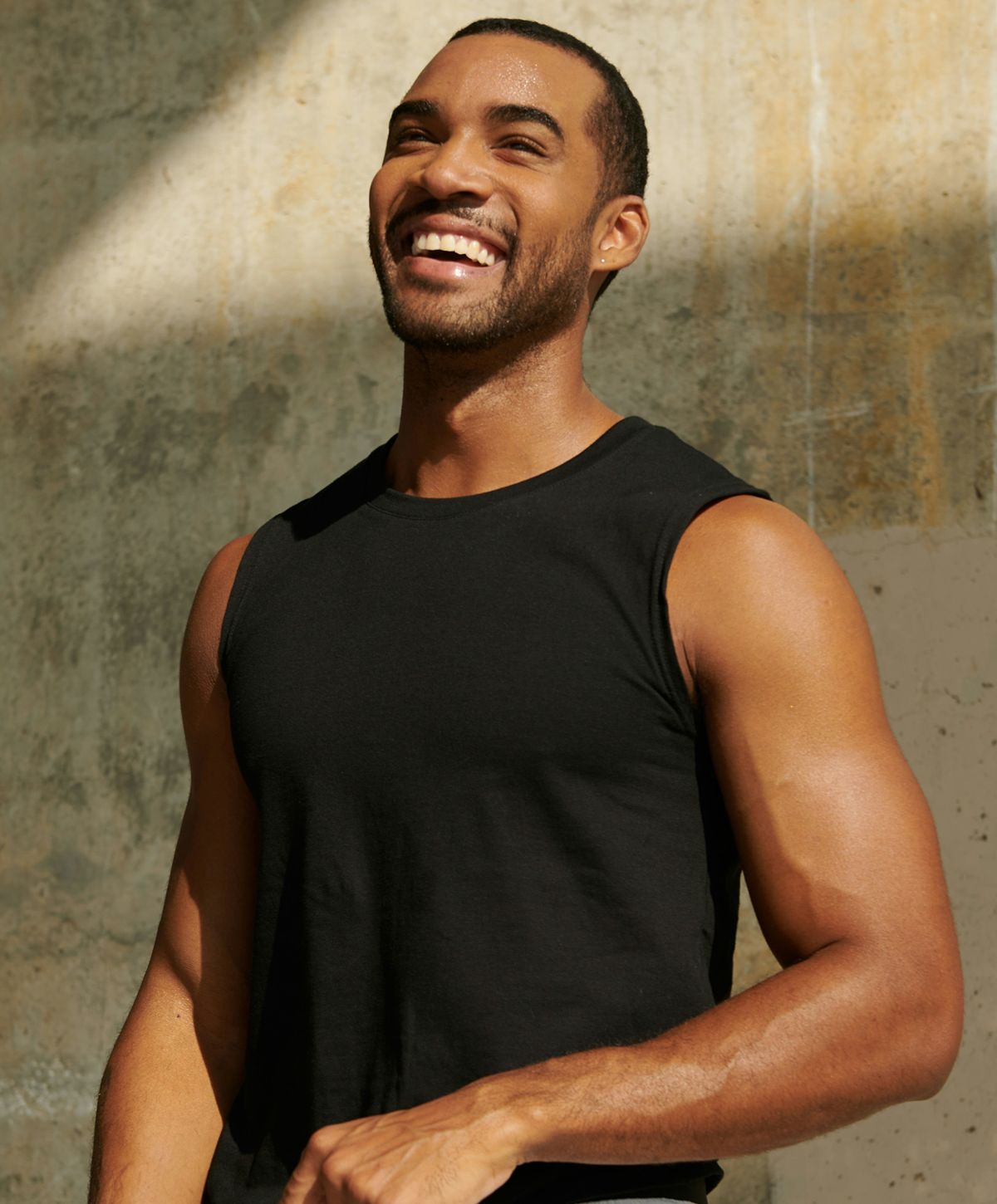 Smiling man in sleeveless shirt against textured background.
