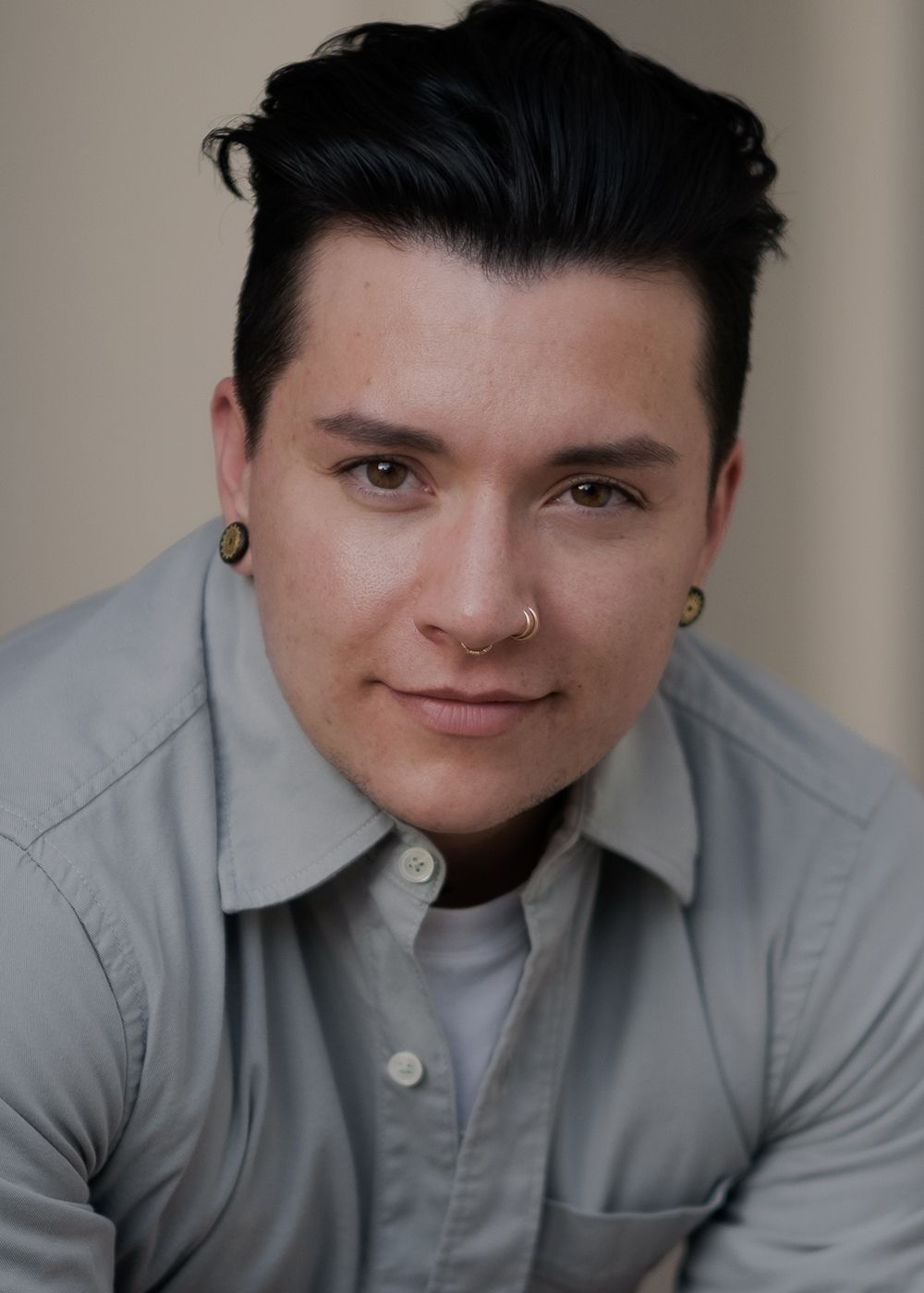 Person with short hair and piercings, smiling.