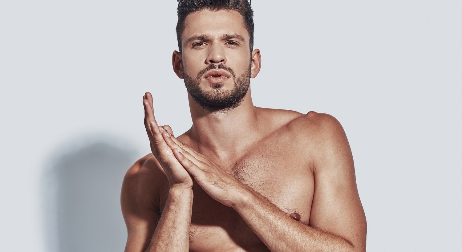 Man posing confidently with serious expression, shirtless.