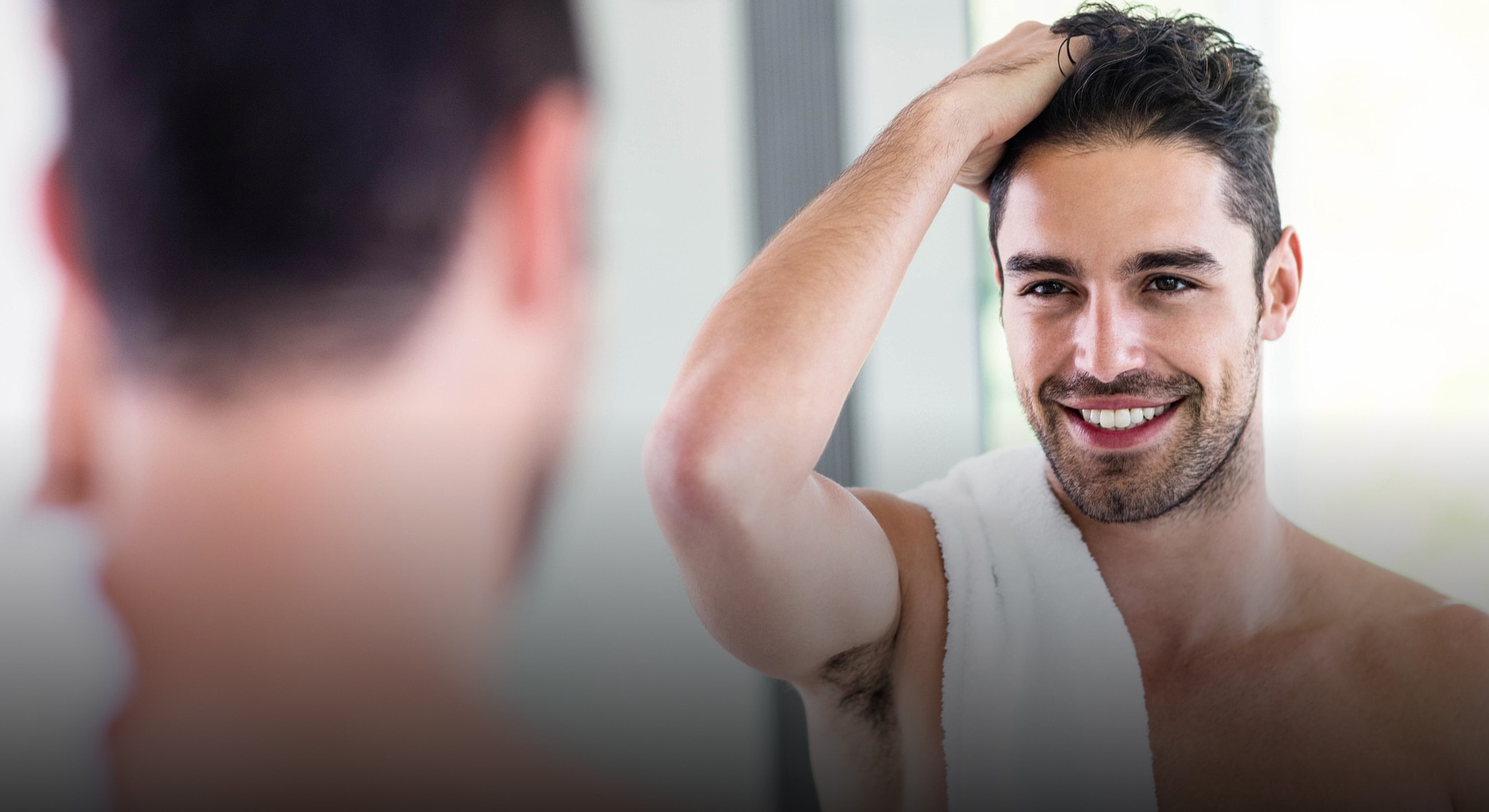 Young man sitting on bed with relaxed expression.